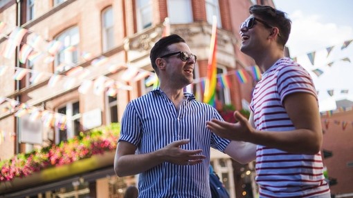 Young male gay couple talking outside a bar in the sunshine.