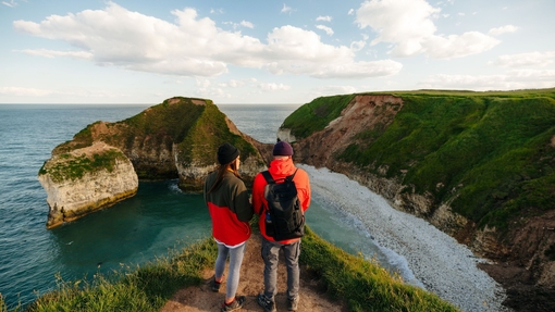 A man and woman stand on a cliff edge in front of a sea view