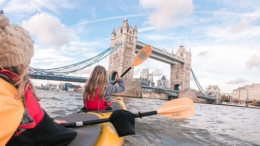 Two women kayaking on the river Thames heading toward Tower Bridge