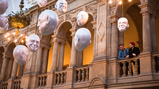 Two men looking at installation of suspended head sculptures