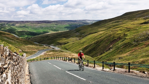 Cyclist riding on road through green dales. Panoramic views