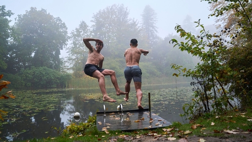 Two men jump off the swimming platform into a lake in an autumnal setting