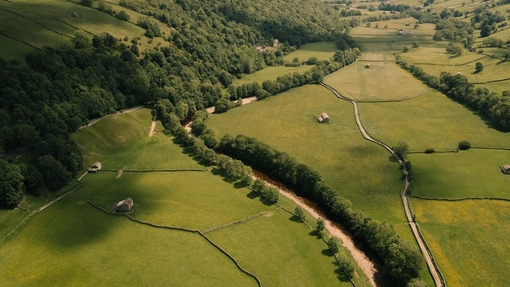 An aerial view of a river surrounded by green fields, trees, and rolling hills.