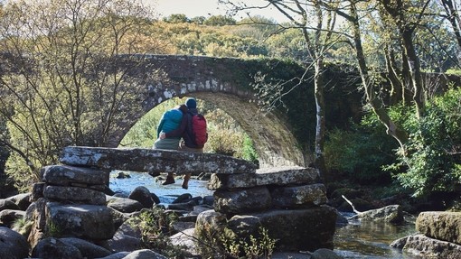 Couple sitting on stone bridge over stream