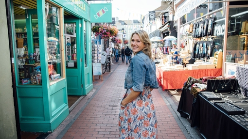 Smiling woman in denim jacket standing between shops
