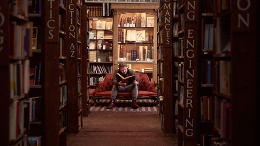 Mann sitzt auf einem Sofa und liest ein Buch in einer Buchhandlung