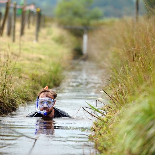 A competitor neck deep in a water-filled trench.