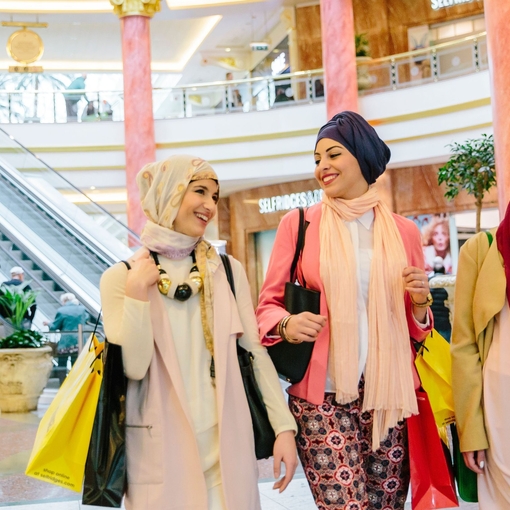 Three women, wearing scarves, walking with shopping bags