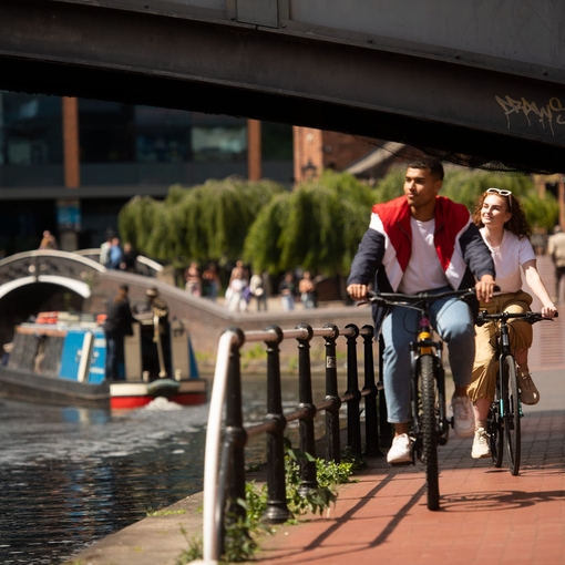 A couple cycling down a ramp parallel with a canal