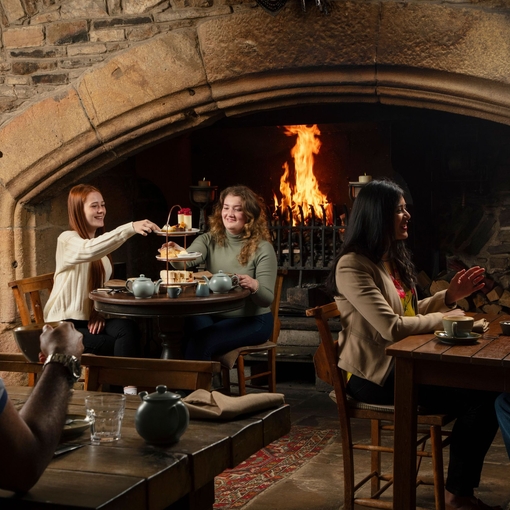 Two women enjoy an Afternoon Tea in front of a fire in an traditional historic pub
