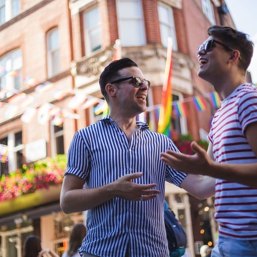 Young male gay couple talking outside a bar in the sunshine.