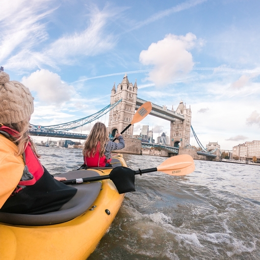 Two women kayaking on the river Thames heading toward Tower Bridge