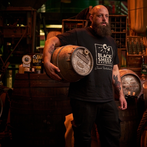 Man standing in store room, holding wooden beer barrel
