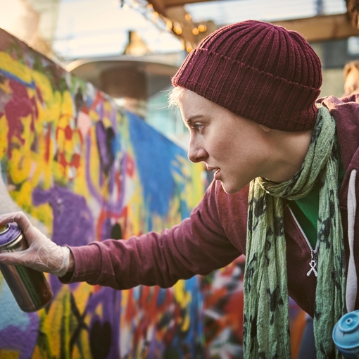 One young woman using aerosol to create street art mural