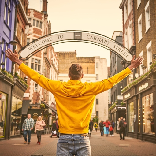 A man posing for the camera in front of a 'Welcome to Carnaby Street' sign in London.