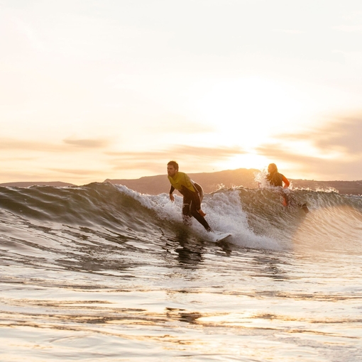 Man and woman, in wetsuits, surfing a small wave