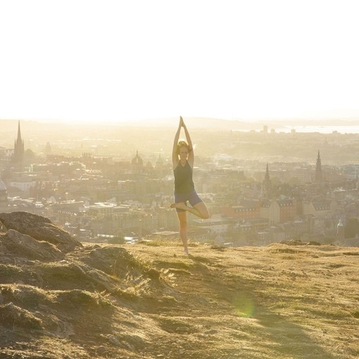 An instructor from Adventure Yoga Edinburgh holds a yoga pose on Arthur’s Seat overlooking the city