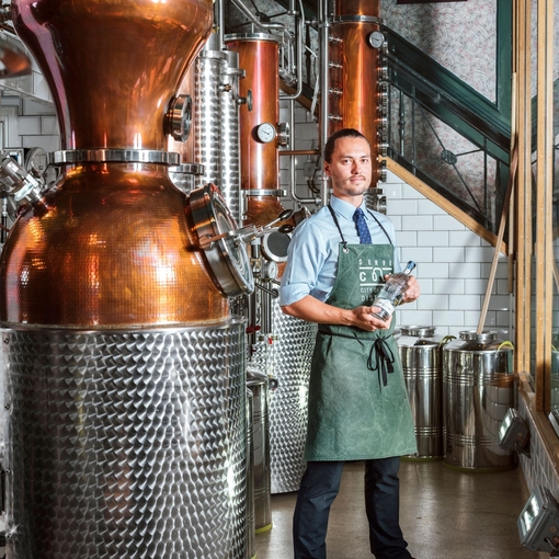 Man wearing green apron standing next to copper pot