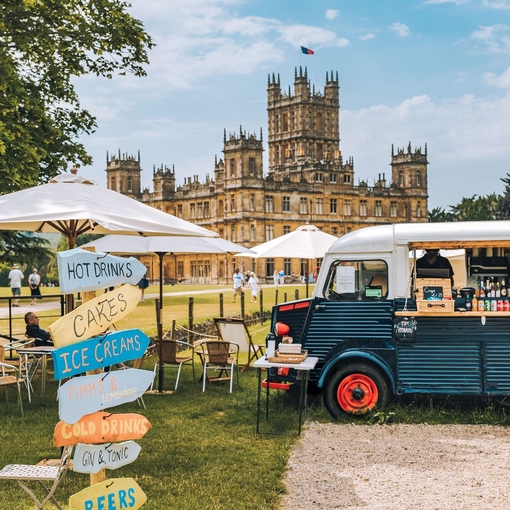 Food truck and direction signs at a festival at Highclere Castle with house behind