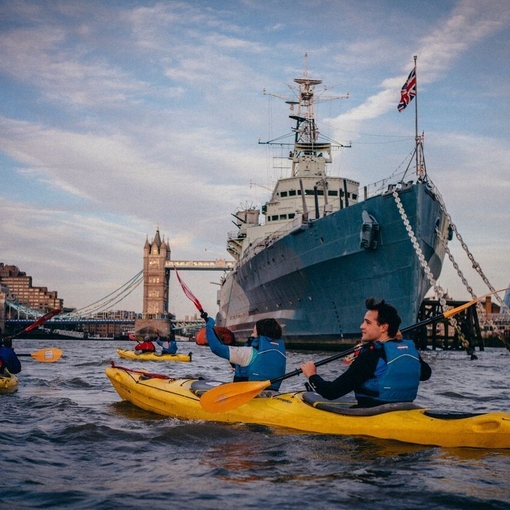 People in Kayaks on river Thames going past HMS Belfast with Tower Bridge in the distance