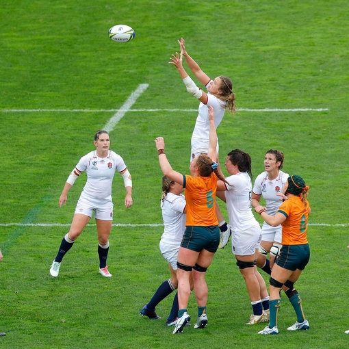 Women's rugby match with players from two teams jumping to catch the ball on the field