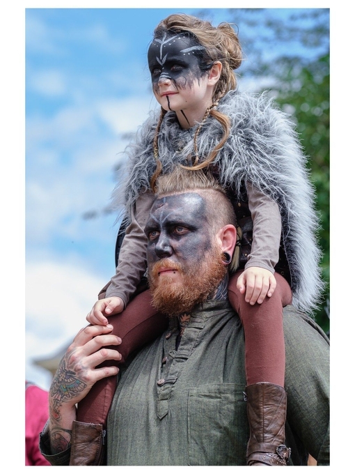 Ein Mann, der ein Kind in Wikingerkostüm und mit Gesichtsbemalung auf den Schultern trägt, im Jorvik Viking Centre, York