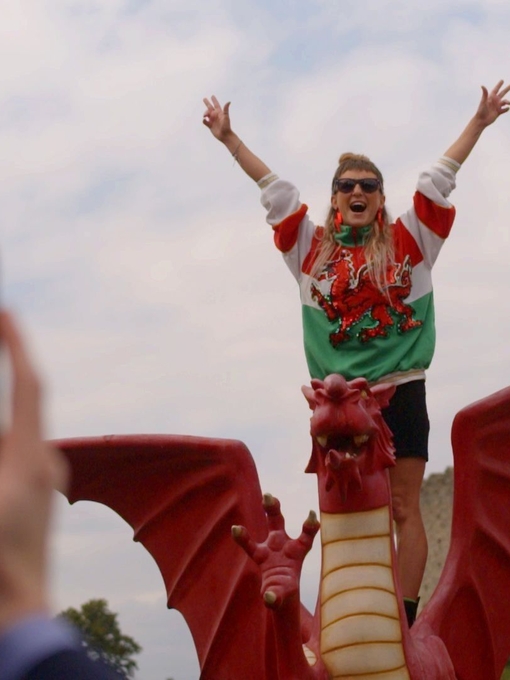 Woman has picture taken standing on a model Welsh dragon.