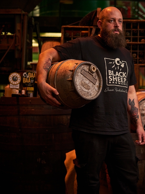 Man standing in store room, holding wooden beer barrel