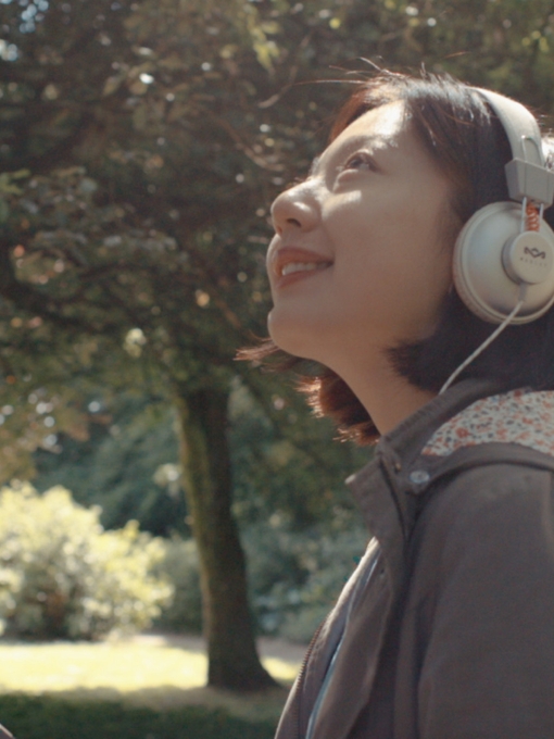 A woman in headphones looking out in a garden at St Fagans National Museum of History, Cardiff