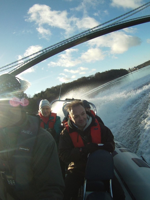 A group of people passing under an iron bridge on a speedboat in Snowdonia/Eryri National Park