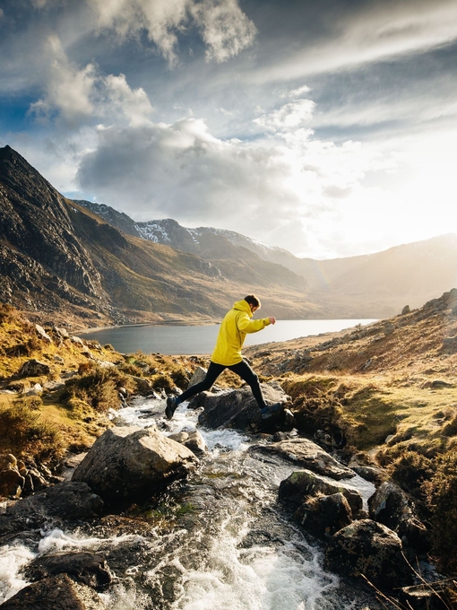 A man jumping across a stream whilst hiking
