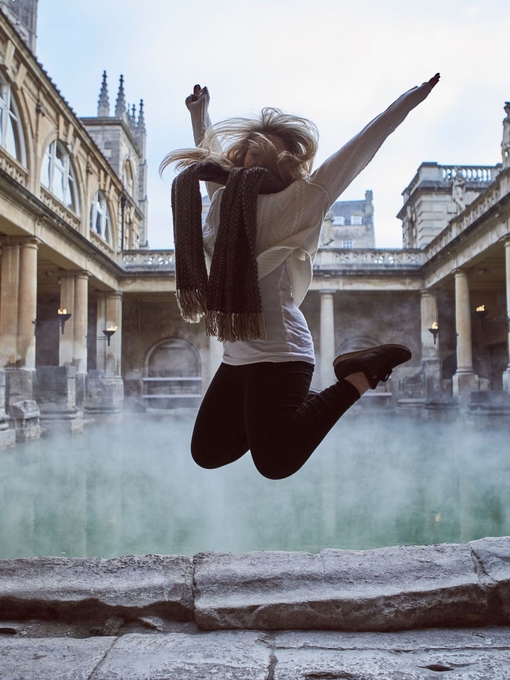 Woman leaping in the air at The Roman Baths, Bath, Somerset, England.
