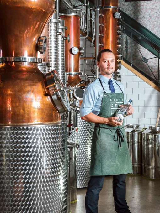 Man wearing green apron standing next to copper pot