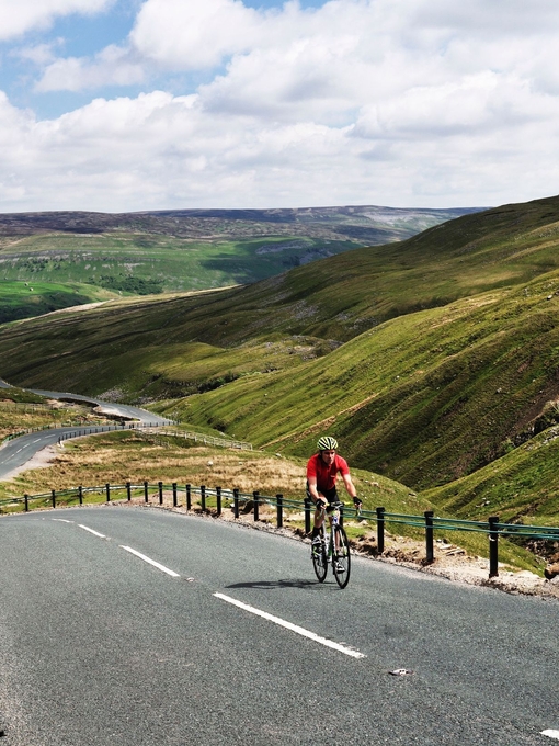 Cyclist riding on road through green dales. Panoramic views