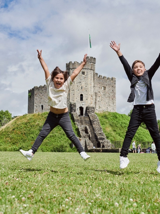 Two children jumping in front of a castle.