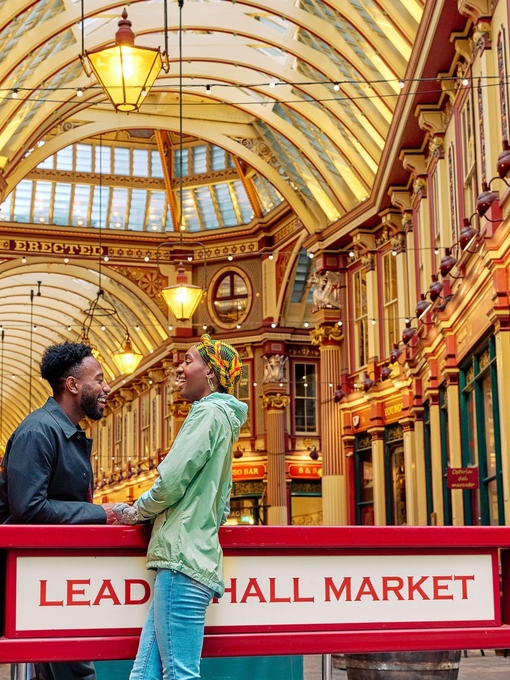 ثنائي مبتسم يتبادل الحديث أمام قاعة سوق ذات سقف ذهبي مزخرف بإتقان.