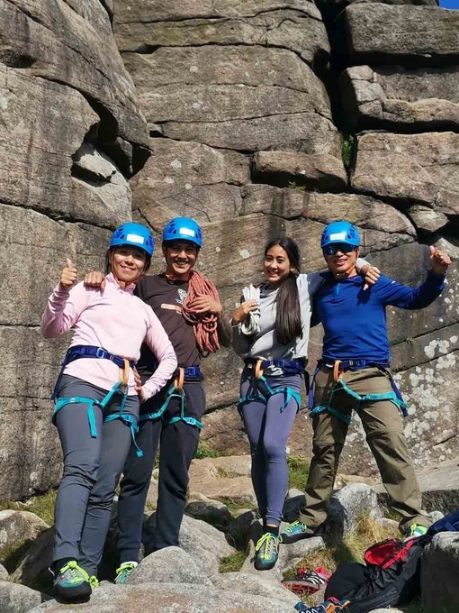 A team of four standing in front of a wall of rock wearing climbing gear