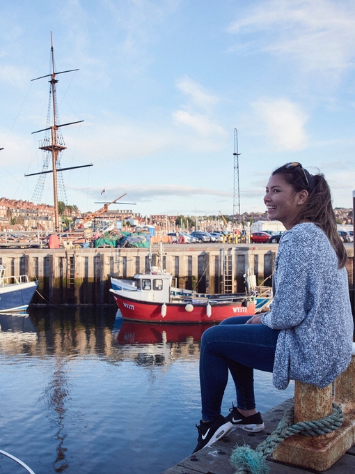 Smiling woman sitting on jetty on Whitby harbour looking at boats