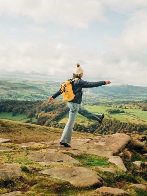 Woman skipping on rocks at edge of hill. Landscape view