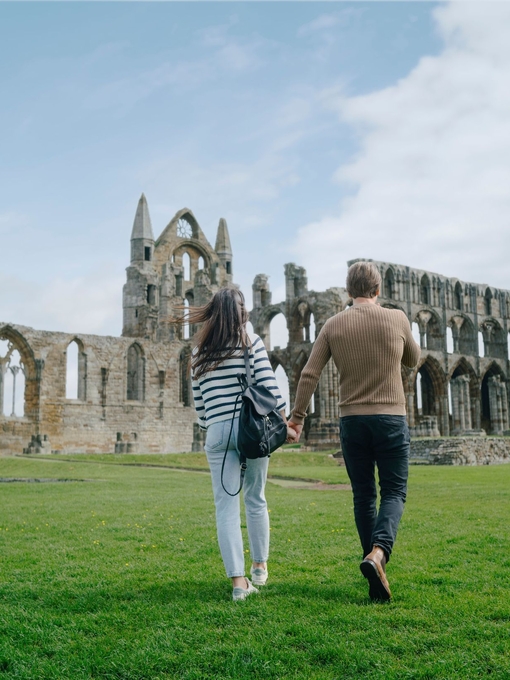 A man and woman walking towards a heritage Abbey building