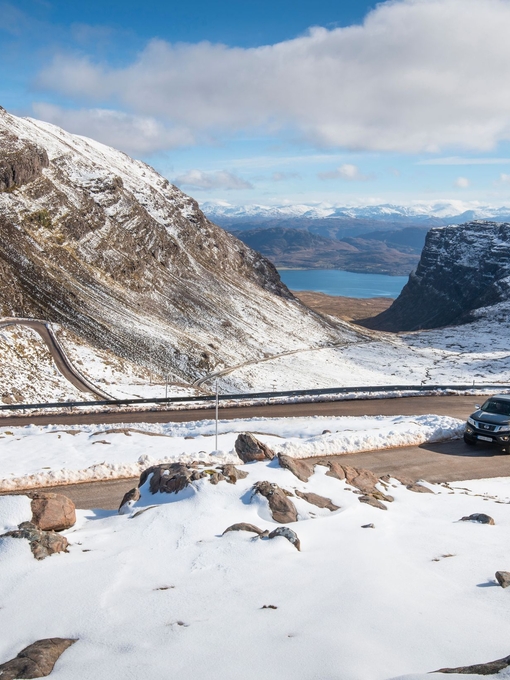 A pickup truck drives up a windy, hilly road lined with snow in winter