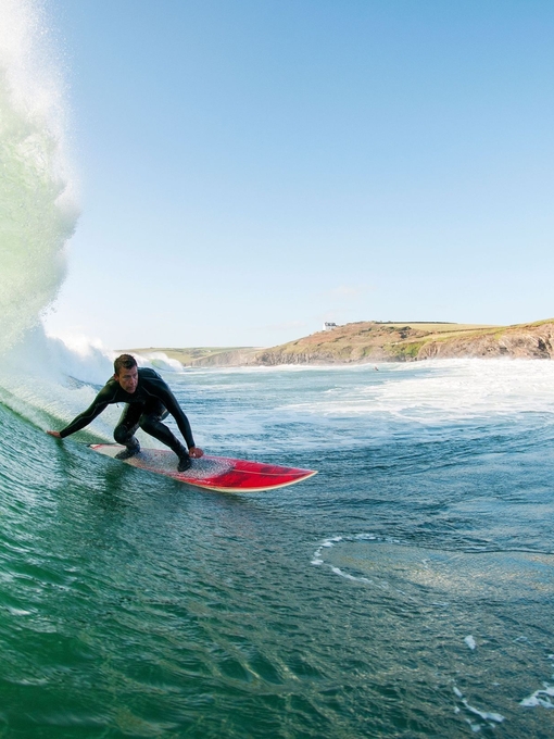 Surfer in a wetsuit surfing a large wave on a red surfboard