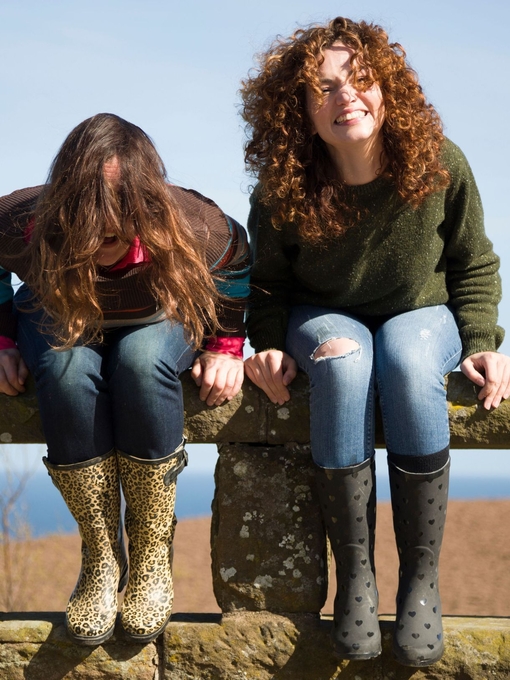 Two cheerful women holding mugs with hot drinks, laughing