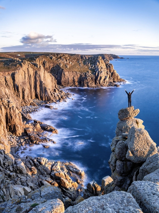 Man standing on a rocky peak on the edge of the coast looking over the headland