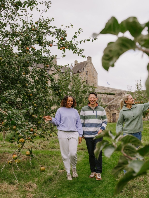 A man and two women walking through an apple orchard on castle grounds.