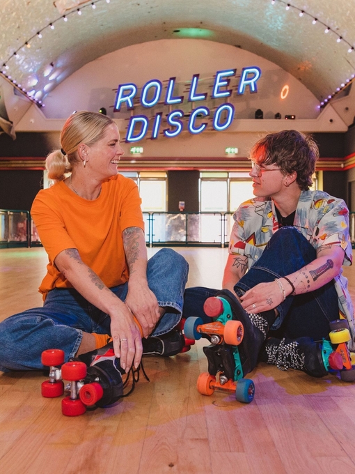 A woman and a man sit wearing roller skates at a Roller Disco