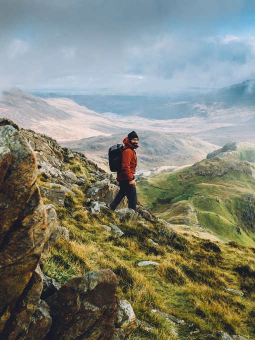A rugged up man navigating the panoramic summit of a large mountain range