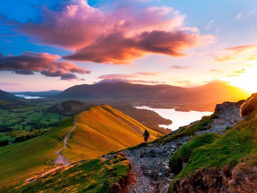 Hiker walking along a path on the mountain ridge at sunset
