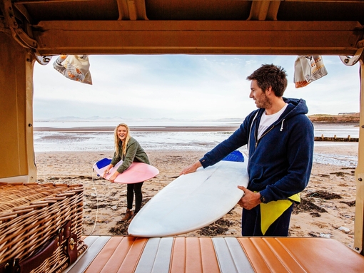 Young man and woman unloading surfboards from camper van
