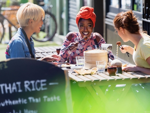 Tre giovani amiche che gustano un pranzo a base di dim sum in un soleggiato caffè sul marciapiede
